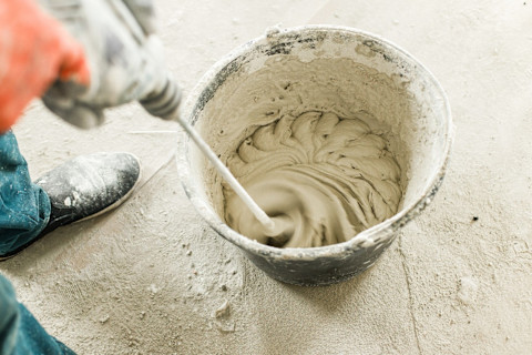 Vakman mengt gipspleister met water in een emmer ter voorbereiding op stucwerk.