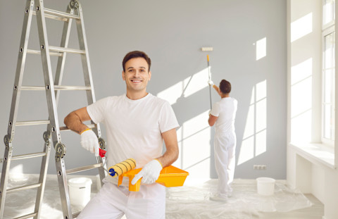 Twee werklieden voeren renovatiewerkzaamheden uit in een appartement met gereedschap en ladders.