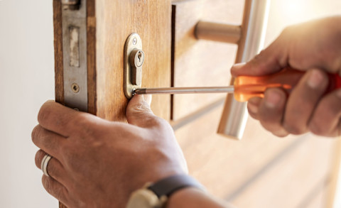 Slotenmaker vervangt een deurslot met gereedschap, close-up van handen en cilinderslot.