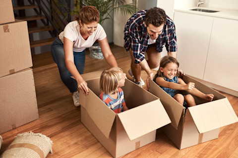 Spelende kinderen en ouders in hun nieuwe huis met verhuisdozen op de achtergrond.