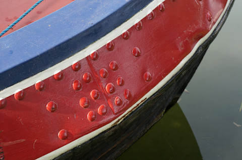 Een schilder brengt een nieuwe verflaag aan op de romp van een boot.
