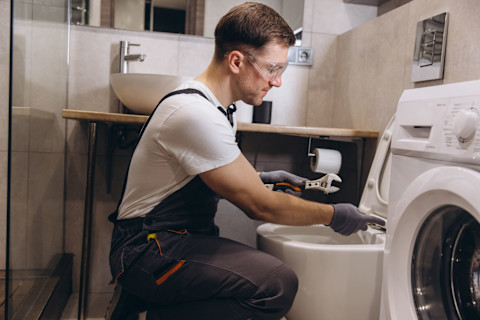 Een vakman zit voor een toilet in een badkamer, hij repareert deze.