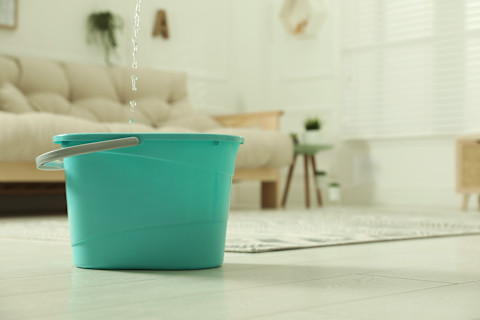 Water lekt uit het plafond in een blauwe emmer vanwege een daklekkage.