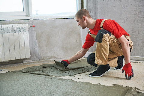 Man aan het werk met het aanbrengen van cement voor een dekvloer.