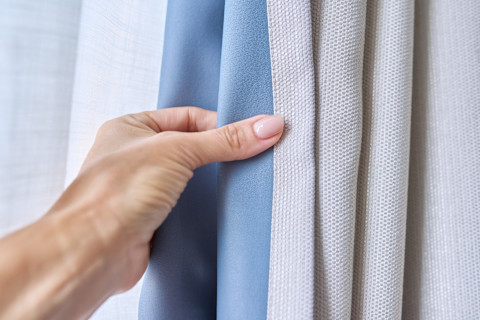 Hand van een vrouw toont een lichtgrijze gordijn met voering voor betere isolatie en een luxueuze uitstraling in je interieur