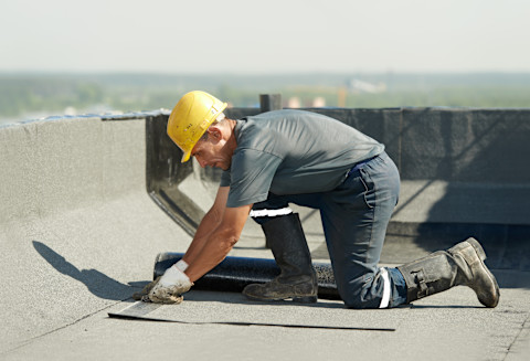 Dakwerker brengt bitumen dakbedekking aan op plat dak, voorbereiding op isolatielaag zichtbaar.