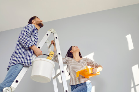 Jong stel schildert samen het plafond in hun nieuwe woning, lachend tijdens de renovatie.