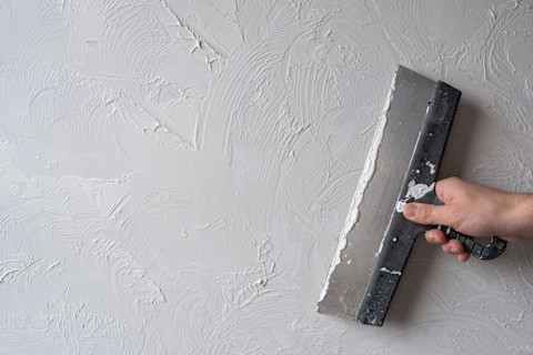 Het aanbrengen van decoratieve witte pleister op een muur, abstracte textuur zichtbaar tijdens het werk.