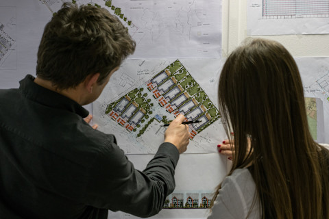 Een man en een vrouw bekijken de bouwplannen van een kleine woning in een wijk