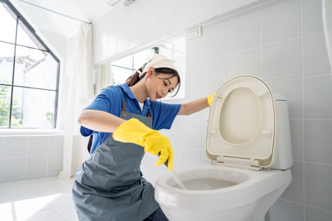 Vrouw in schoonmaakkleding reinigt een toilet met focus op hygiëne. 