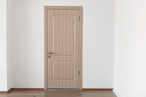 Houten binnendeur in gesloten positie tegen een witte muur, minimalistisch interieur.