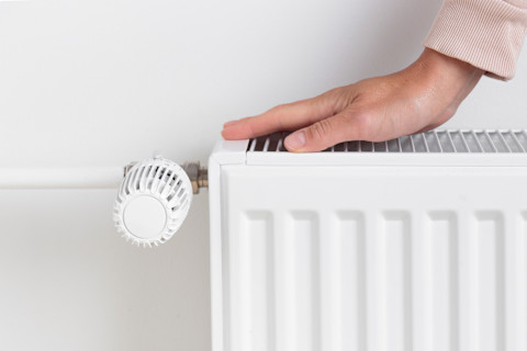 Persoon warmt haar handen op bij een radiator tijdens een koude dag.
