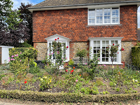 Cottage met kleurrijke voortuin vol bloemen, symmetrisch aangelegd met een natuurlijke uitstraling.