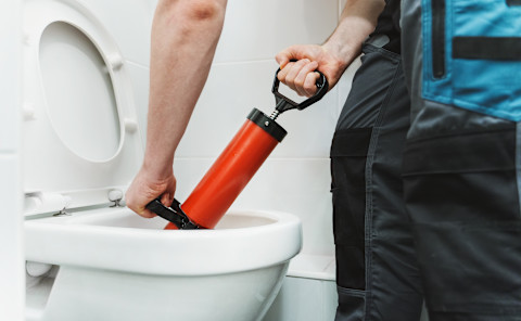 Een loodgieter gebruikt een pomp apparaat om een wc te ontstoppen