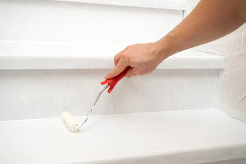  Een hand schildert een trap met witte verf.