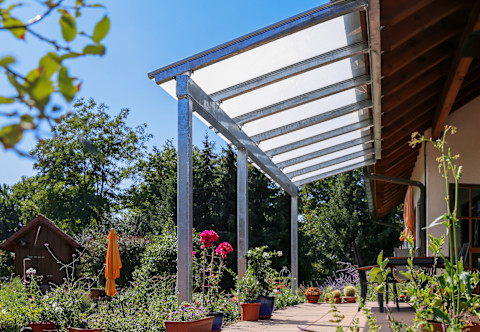 Overdekt terras met glazen dak en uitzicht op groene tuin, ideaal voor elk seizoen.  
