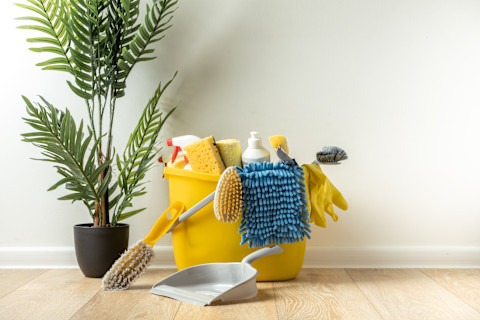 Schoonmaakmaterialen zoals borstels, flessen met reinigingsmiddelen, sponzen en een doek op een witte achtergrond.