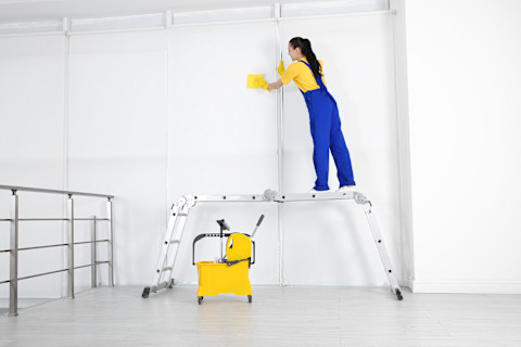 Schoonmaker veegt een muur schoon met een doek na werkzaamheden.