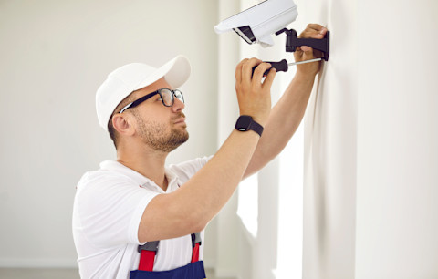 vakman hangt een beveiligingscamera op aan de buitenkant van een witte woning