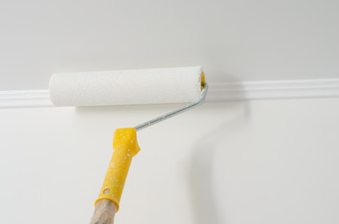 Gele verfroller aan het werk tegen een wit plafond met lichte structuur.