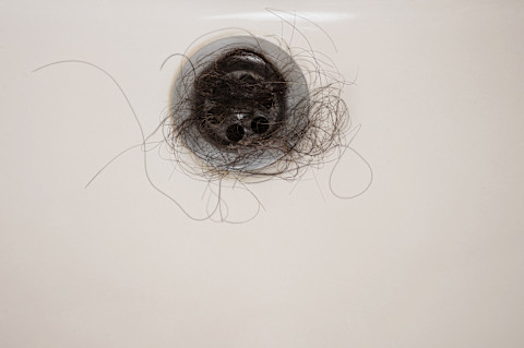 Gootsteen verstopt met donkere haren, duidelijk zichtbaar in de afvoer.
