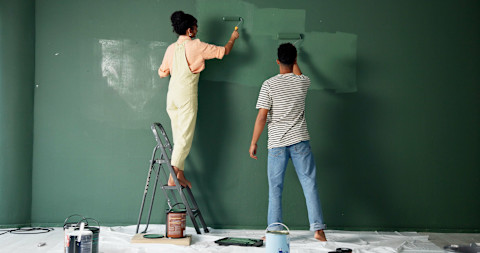 Koppel verft samen een muur met een roller tijdens een huisrenovatie, met vrolijke sfeer.