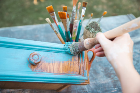 Hand brengt krijtverf aan op houten meubelstuk tijdens een DIY-renovatieproject.