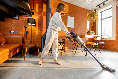 Vrouw maakt een betonvloer schoon met een draadloze handstofzuiger, focus op hygiënisch onderhoud.