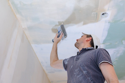 Bouwvakker kijkt omhoog naar net gestuct plafond in woning.