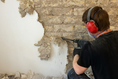 Man boort in de muur om spachtelputz te verwijderen en deze te repareren.