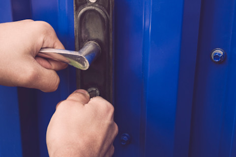 Man probeert het slot open van een blauwe deur open te maken met een sleutel