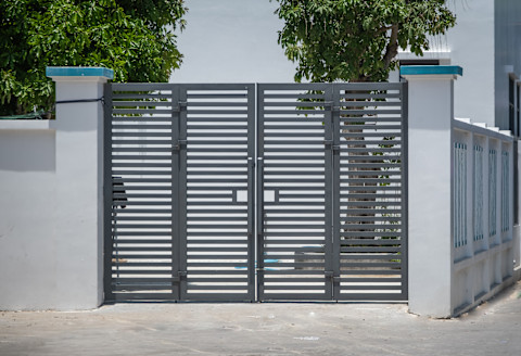 Elektrische poort bij een moderne woning, met aparte doorgangen voor voetgangers en auto's.
