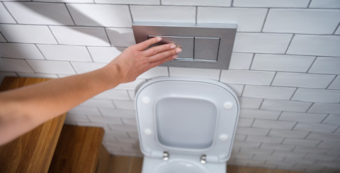 Vrouw drukt op de spoelknop van het toilet.