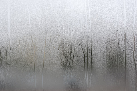 Condensdruppels op een raam na een hevige regenbui, met wazig uitzicht naar buiten en beslagen glas.