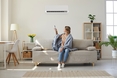 Vrouw zit op een bank onder een airco en geniet van koele lucht in een moderne woonkamer.