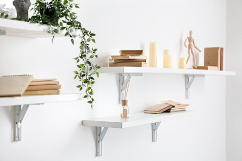 Een aantal witte planken op een muur met decoratieve elementen zoals kaarsjes en planten