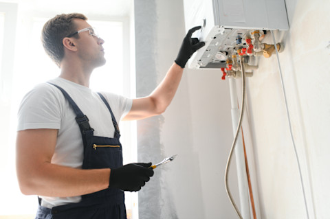 Loodgieter werkt aan de installatie van een witte boiler aan de muur