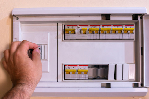 Hand van een installateur inspecteert een moderne groepenkast met bedrading en schakelaars.