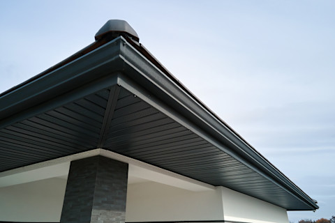 Hoek van een huis met bruine metalen plankensiding en een regenpijp, close-up op gevelmateriaal.