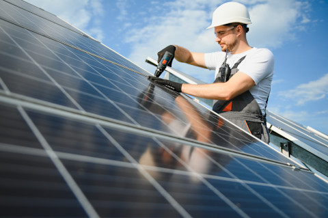 Technicus installeert zonnepanelen buiten tegen een helder blauwe lucht.
