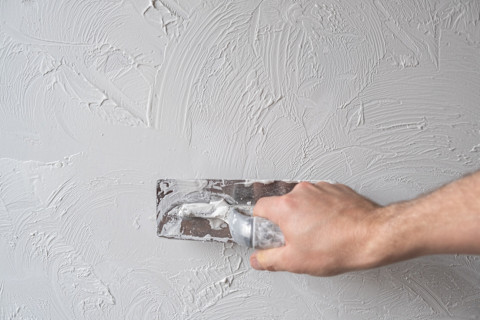Stukadoor brengt witte spachtelputz aan op een muur met een spaan
