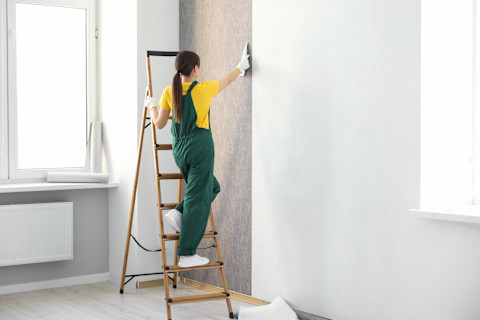 Vrouw gladstrijkt behang op een muur voor een strakke afwerking.