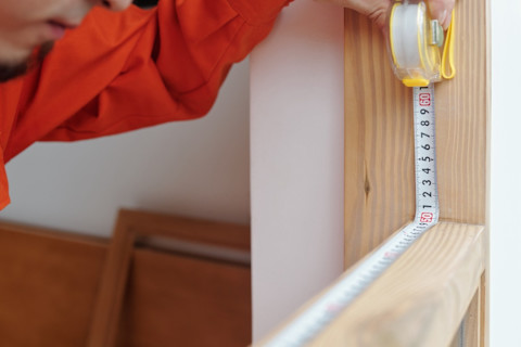 Timmerman meet een houten raamframe zorgvuldig in met een meetlint.
