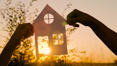 Handen houden een miniatuurhuisje vast op gras, symbool voor een droomhuis of het kopen van een woning