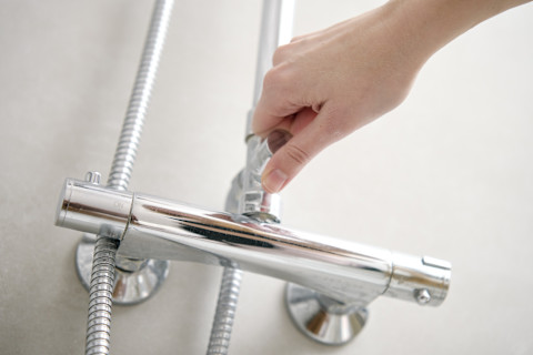 Vrouwelijke hand draait een douchekraan open in een moderne badkamer.  