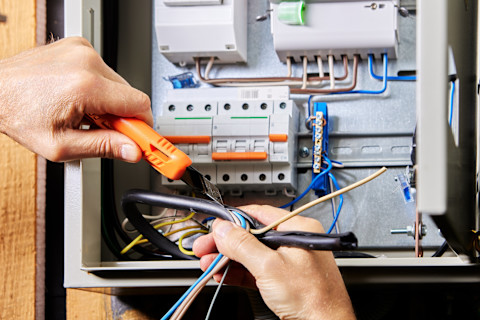 Elektricien sluit een 3-fase stroominstallatie aan in een meterkast met verschillende kabels en aansluitingen.