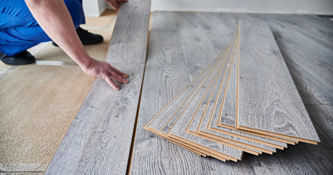 Ervaren vloerspecialist legt grijze laminaat vloer op een houten ondervloer