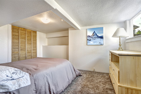 Gezellig slaapkamerinterieur met laag plafond en zachtbruin kleurenpalet.
