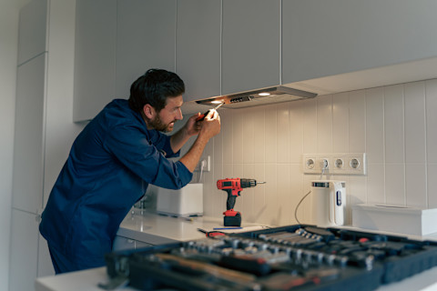 Monteur in uniform installeert een moderne inbouw afzuigkap in een witte keuken.
