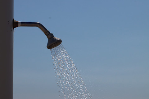 Buitendouche met vallende waterdruppels op een zonnig strand, symbool voor goede waterdruk.